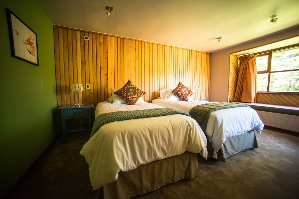 Hotel room at Yelcho with two single beds, wood-paneled walls and a window onto the garden
